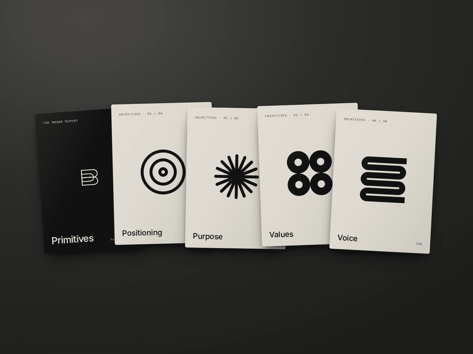 A printed deck of five cards splayed on a dark table: a black Primitives cover card and four linen cards, one mark each for positioning, purpose, values and voice.
