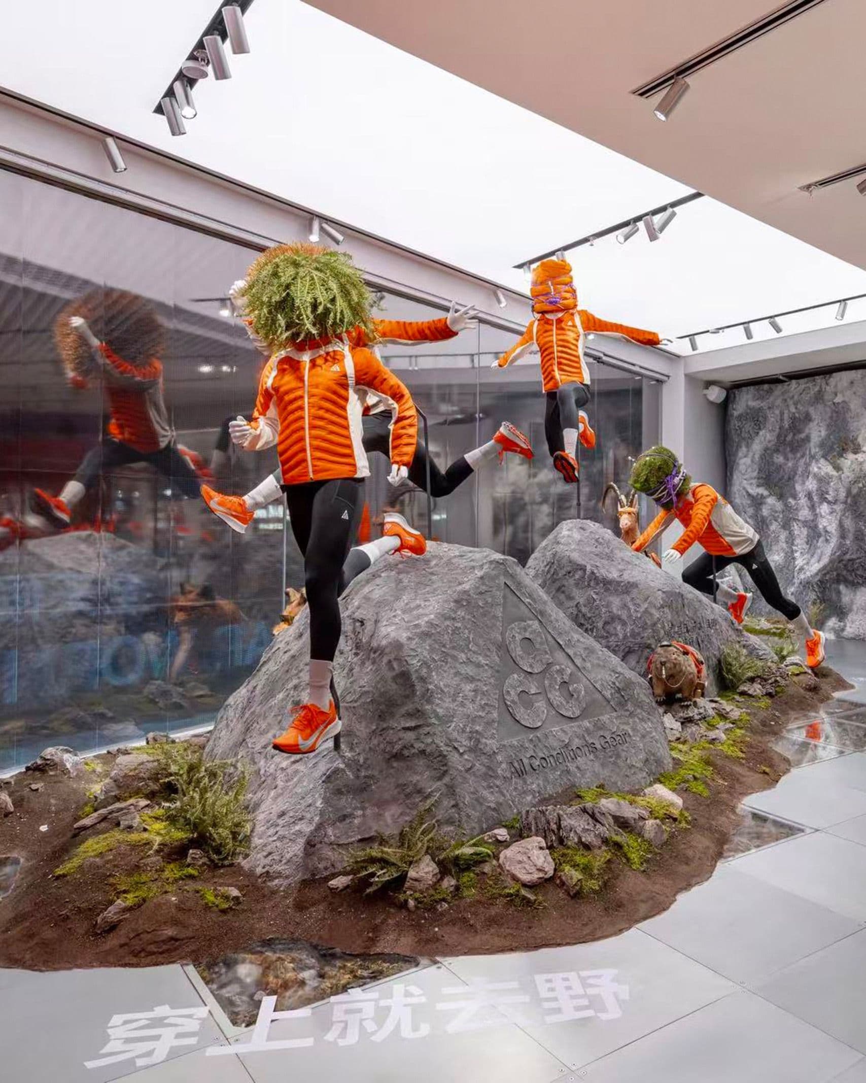 Mannequins in ACG orange leaping across a boulder on a grass plinth inside the Beijing store, Chinese wall type behind
