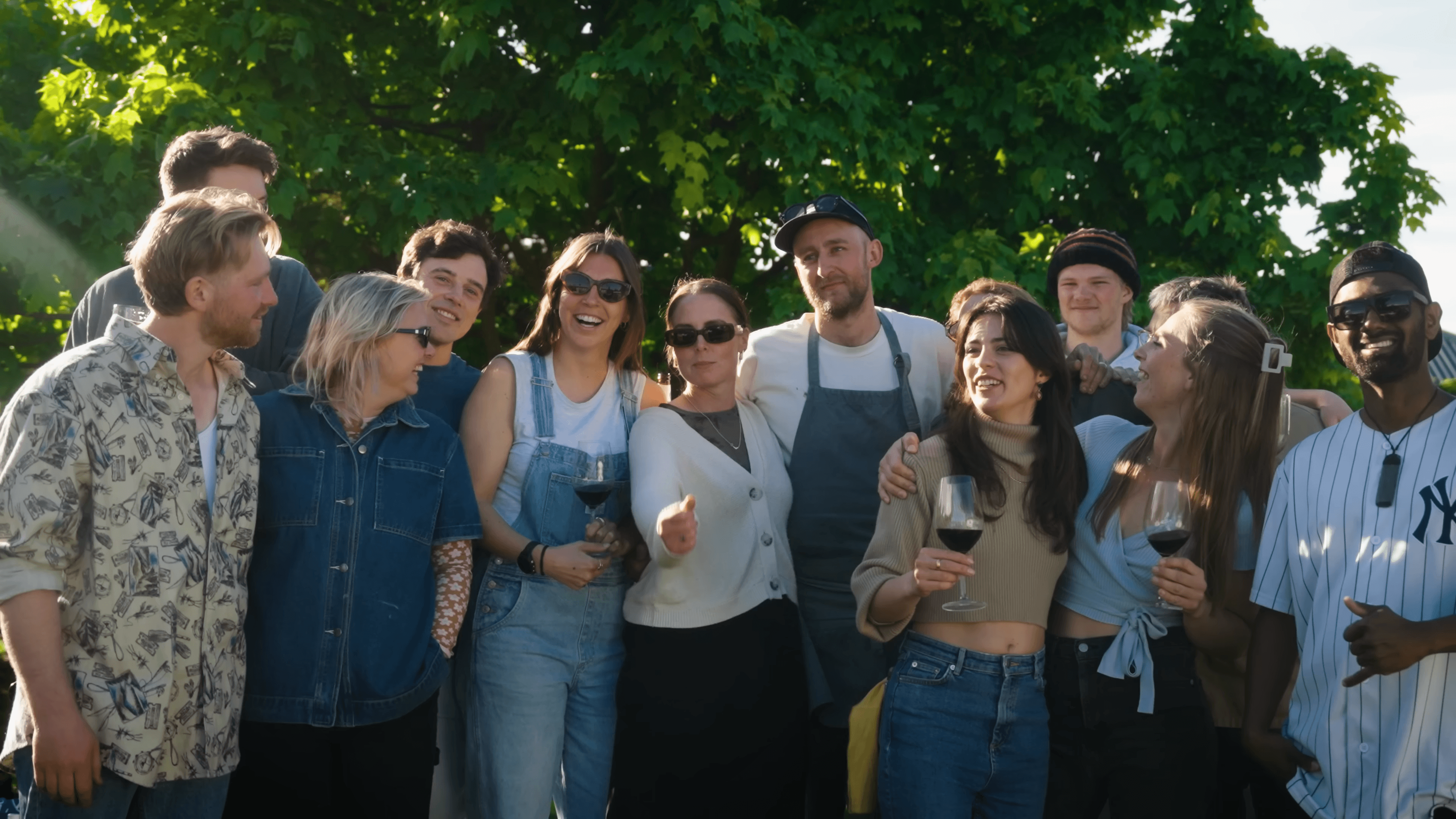 A group of friends with wine glasses, laughing together under a tree in late sun