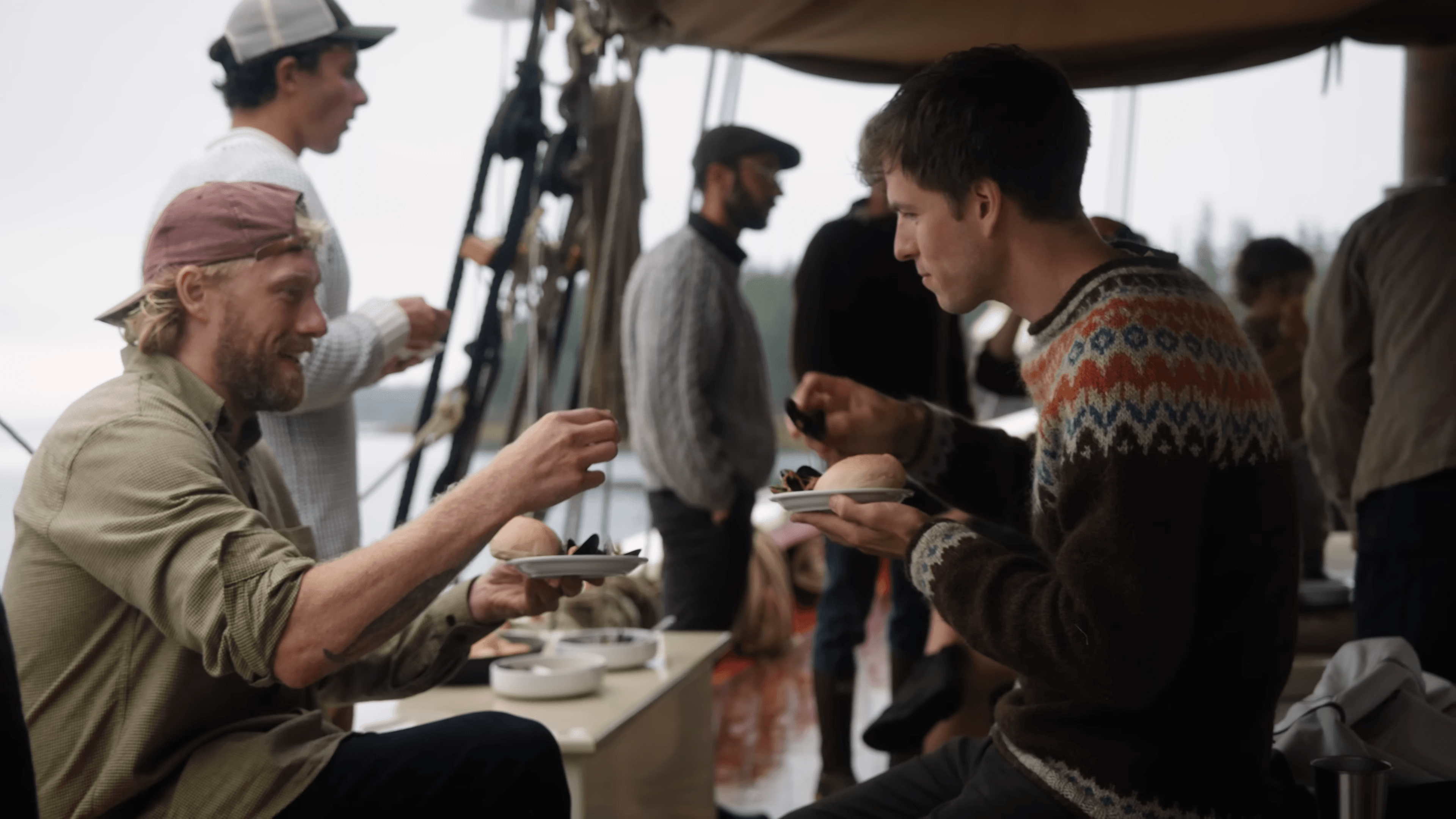 People in sweaters passing plates on the deck of a schooner on a foggy morning