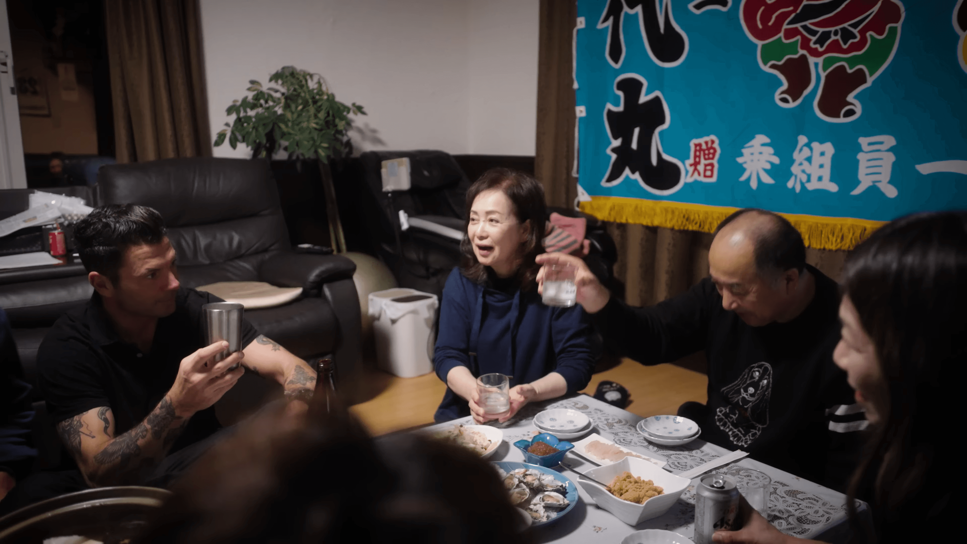 Fishermen and their families raising glasses around a low table, a crew banner in Japanese on the wall