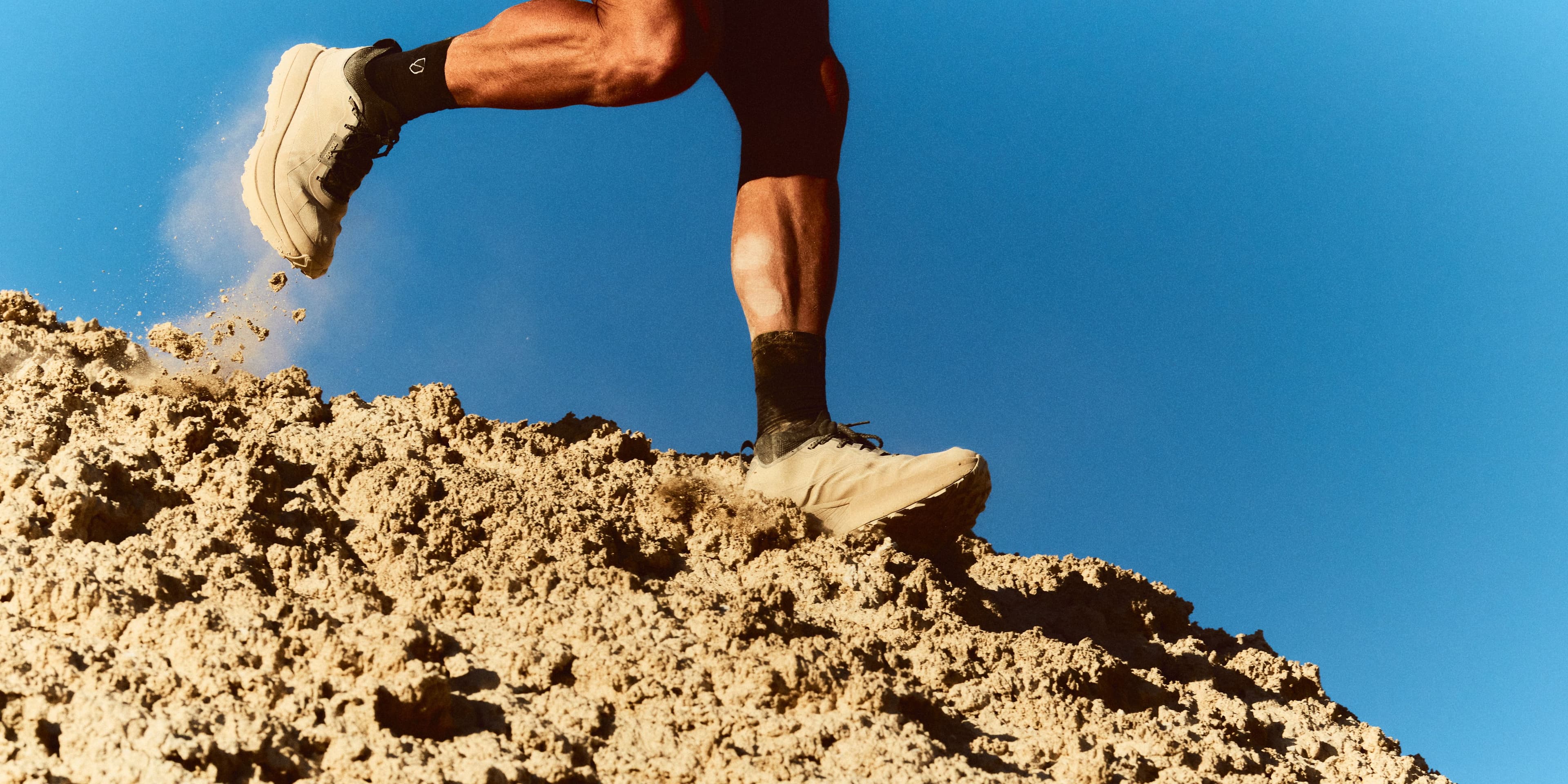 A runner crests a sand ridge against a hard blue sky, one 055 kicking up dust