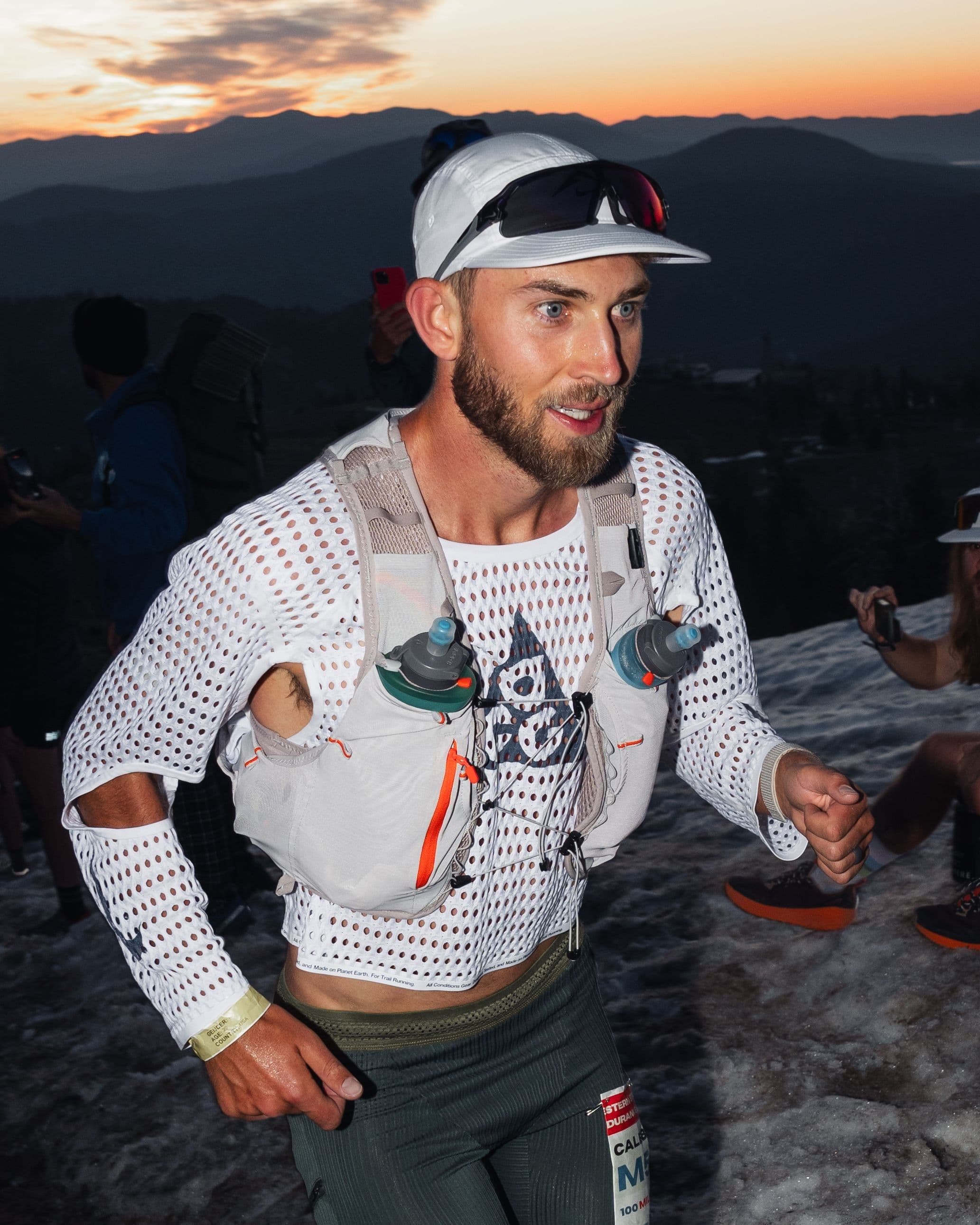 Caleb Olson at dawn on the Western States course in the white prototype and a race vest, mountains behind