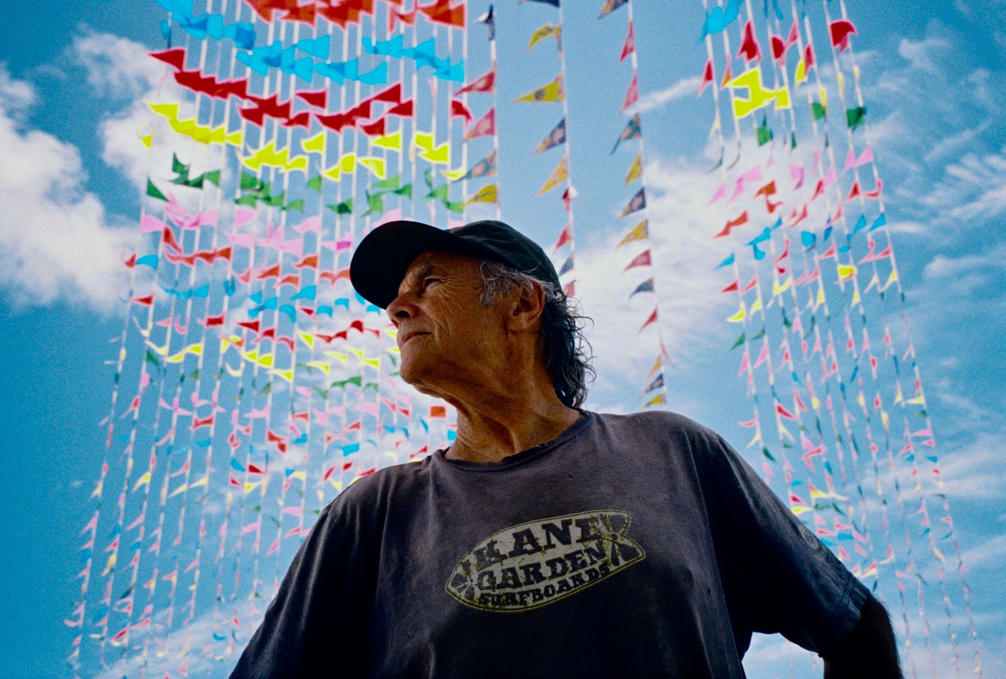 David Carson photographed from below against a bright blue sky, strings of multicoloured bunting behind him.