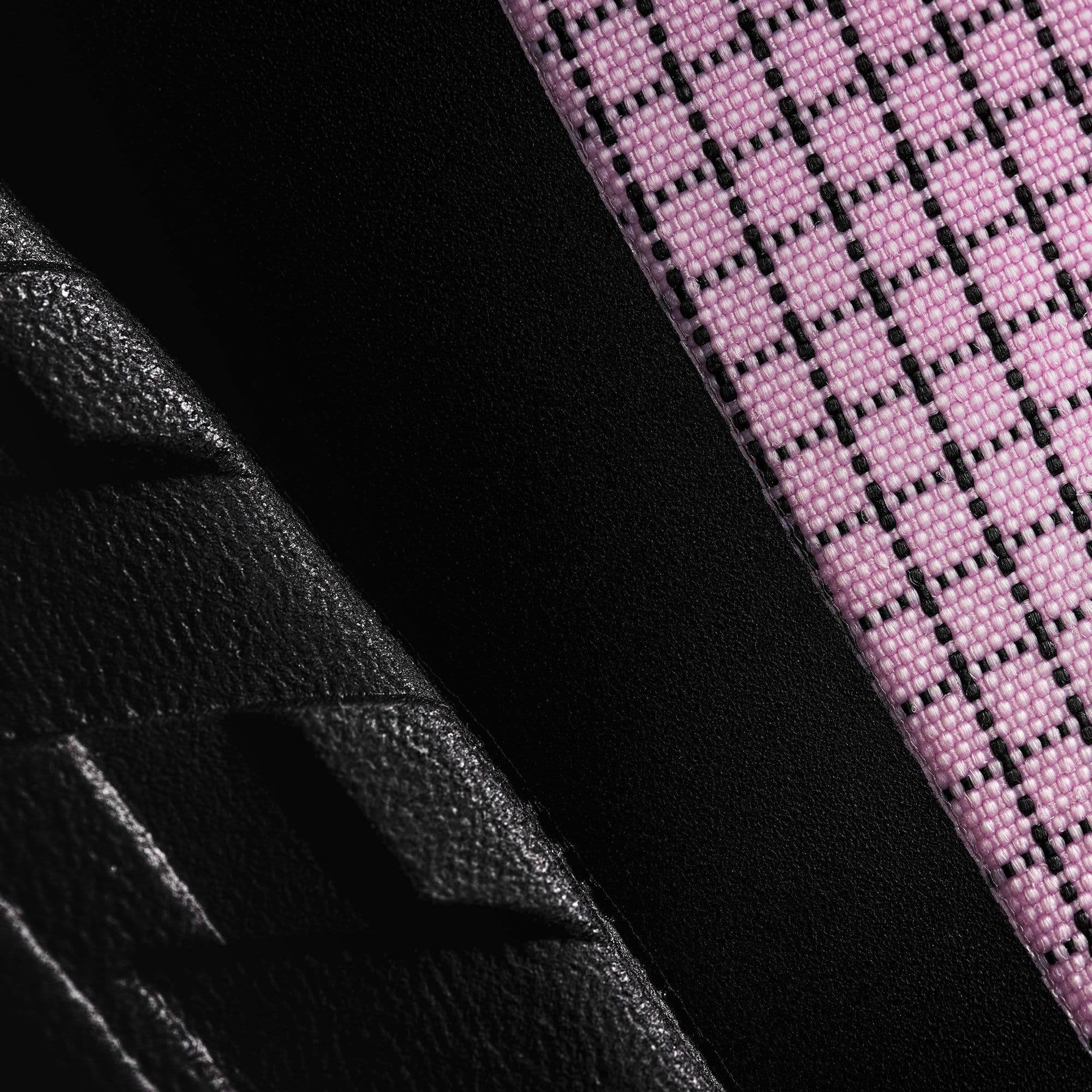 Close up, a pink woven fabric with a black grid beside black textured rubber