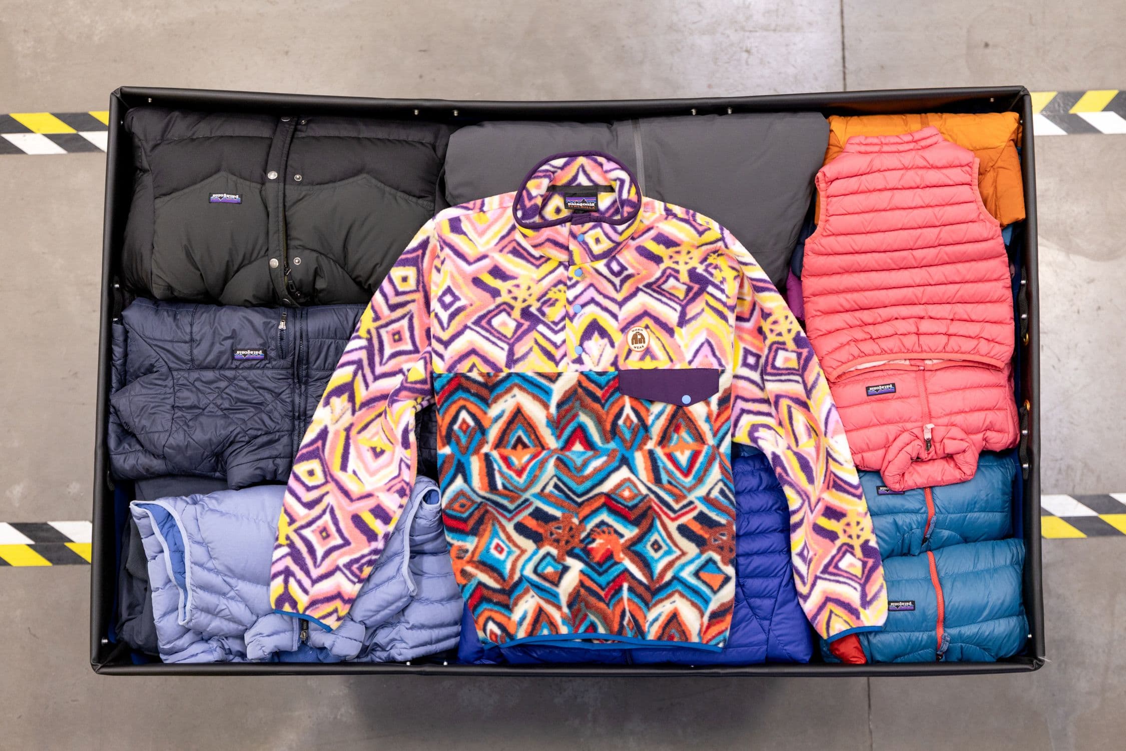 Overhead view of a sorting bin at Patagonia’s Reno facility: a geometric-print Snap-T fleece laid over folded puffer jackets and vests.