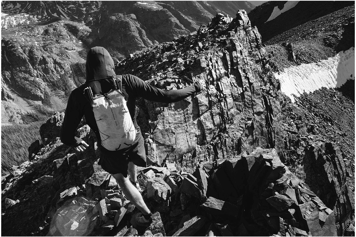 Black and white: a runner with a pale pack scrambles up broken rock beside a snow band