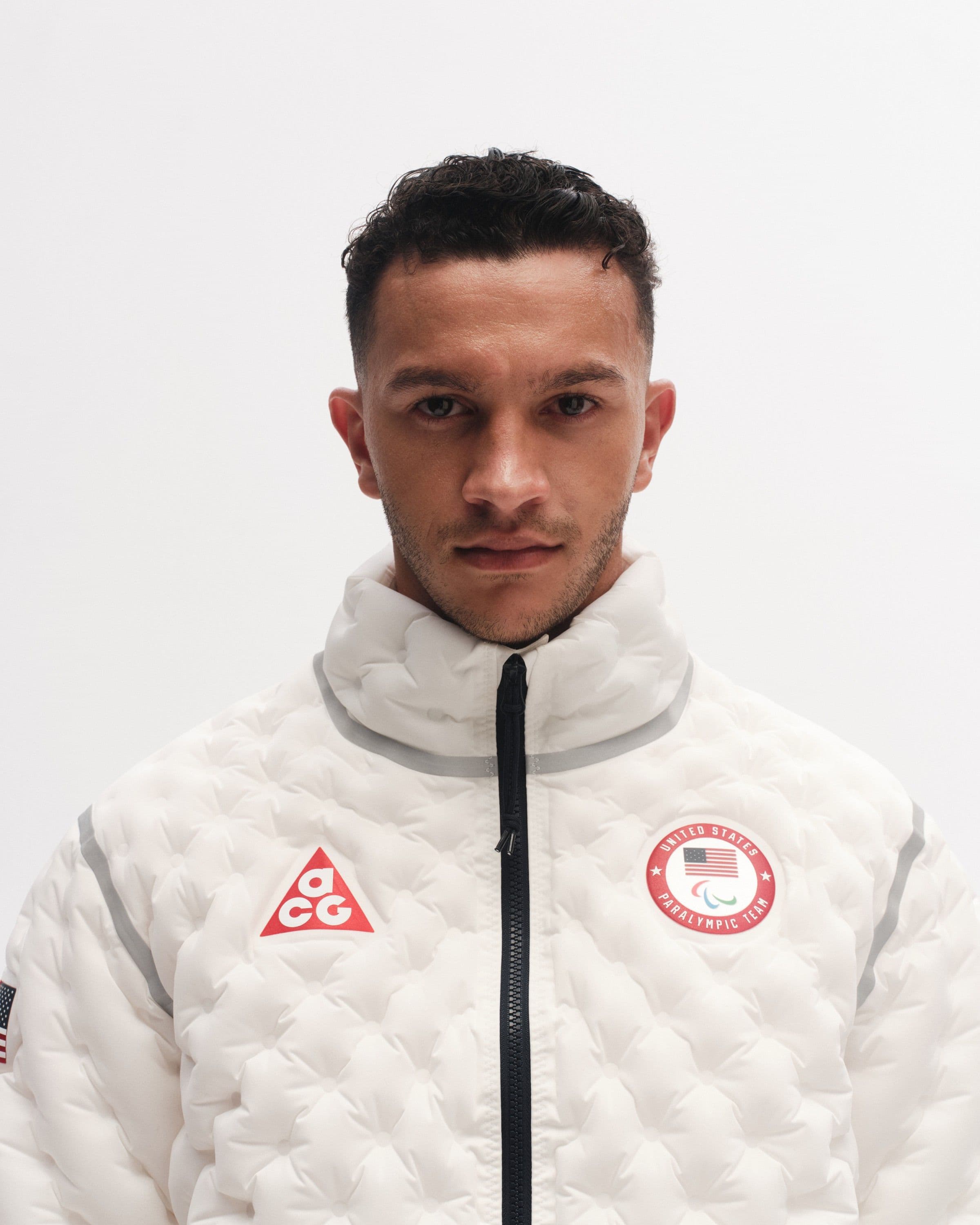 A man in a white quilted jacket with a red ACG triangle on one side of the chest and the Team USA crest on the other