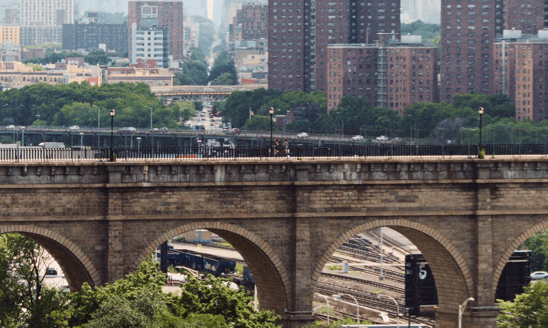 Two runners on the High Bridge walkway, stone arches over rail yards, Harlem's towers behind