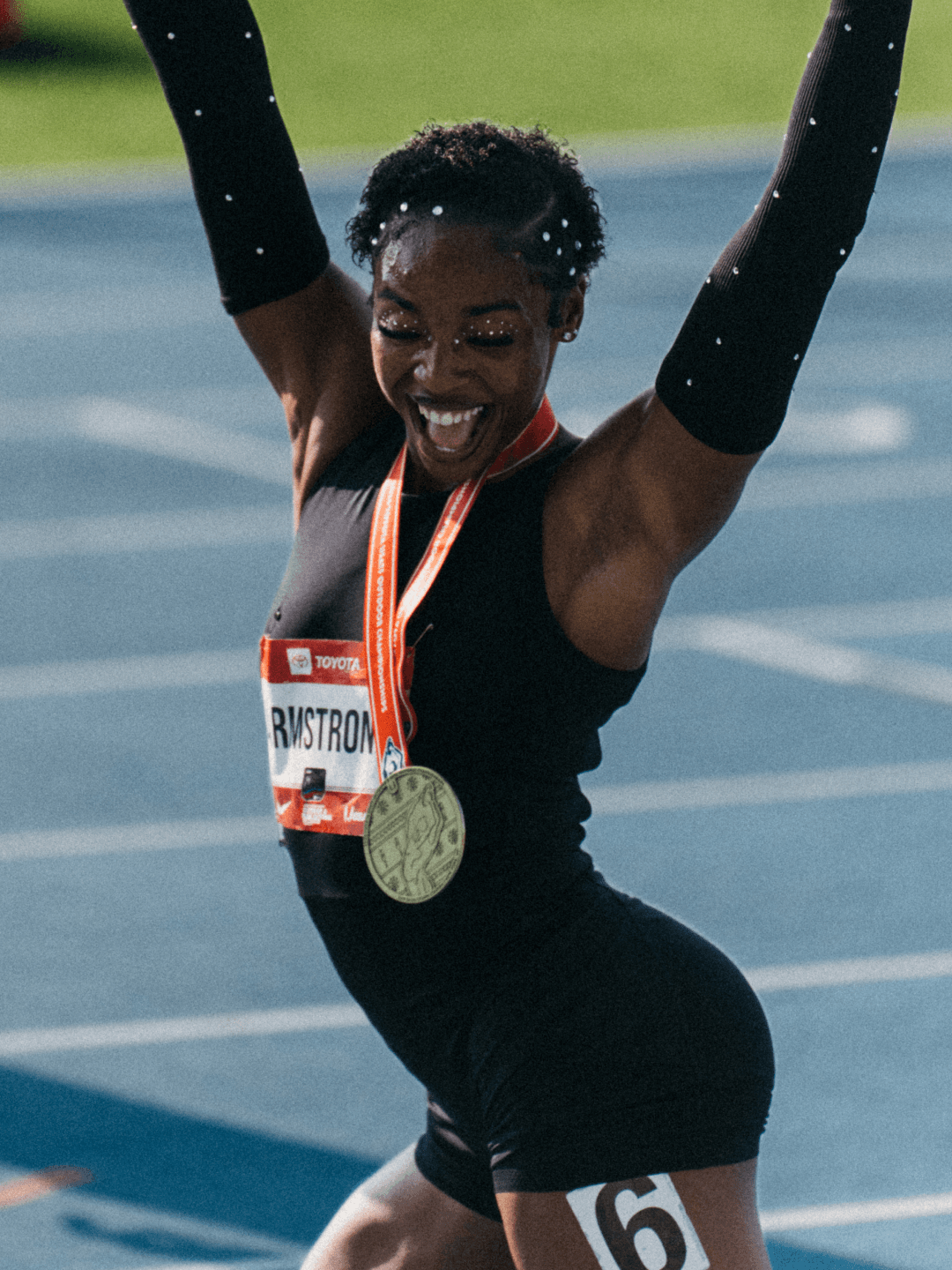 Armstrong with her arms up and a gold medal round her neck, shouting with joy on the blue track