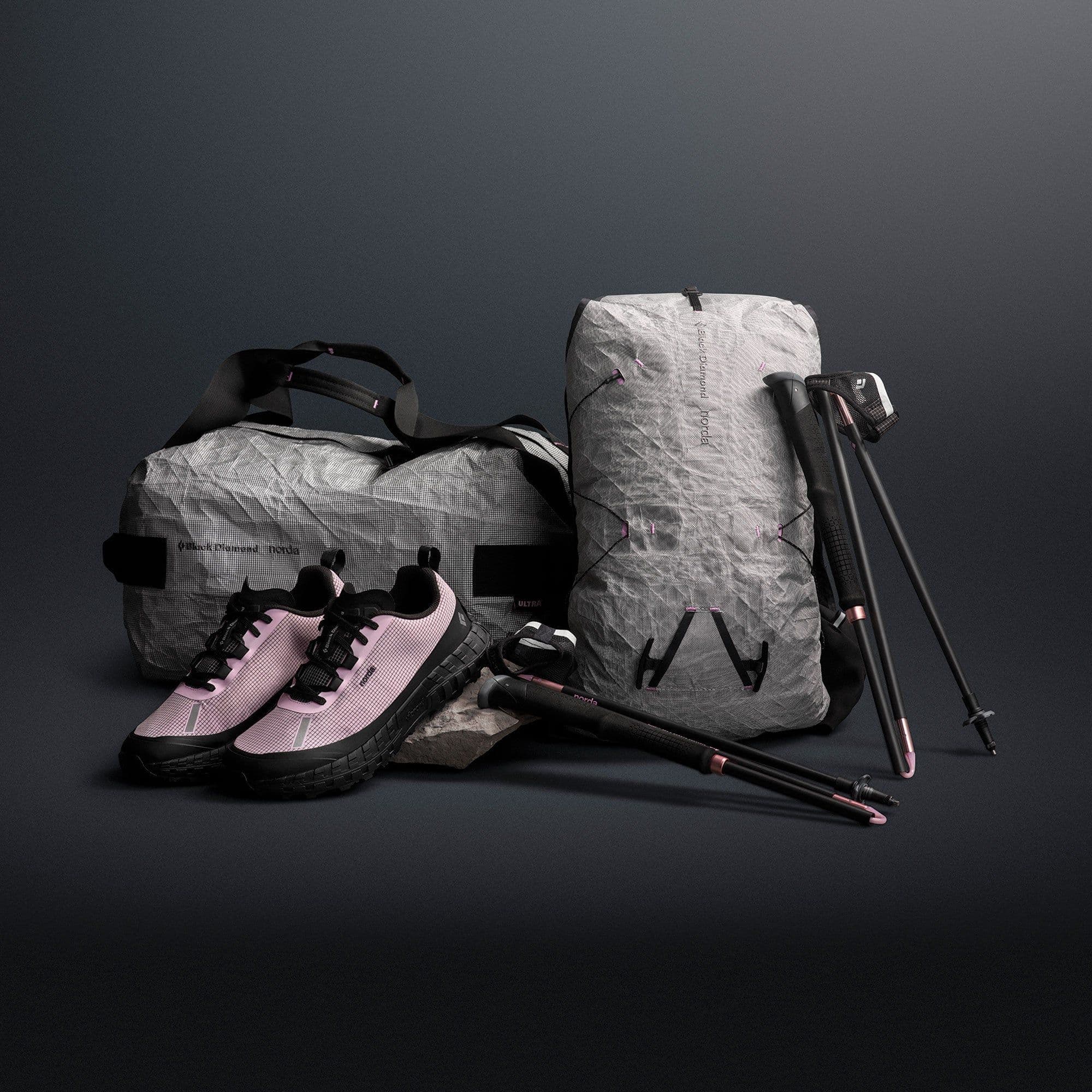 The collection on a dark ground: pink and black shoes, a pale grey duffel and pack in crinkled sailcloth, and black poles with pink details