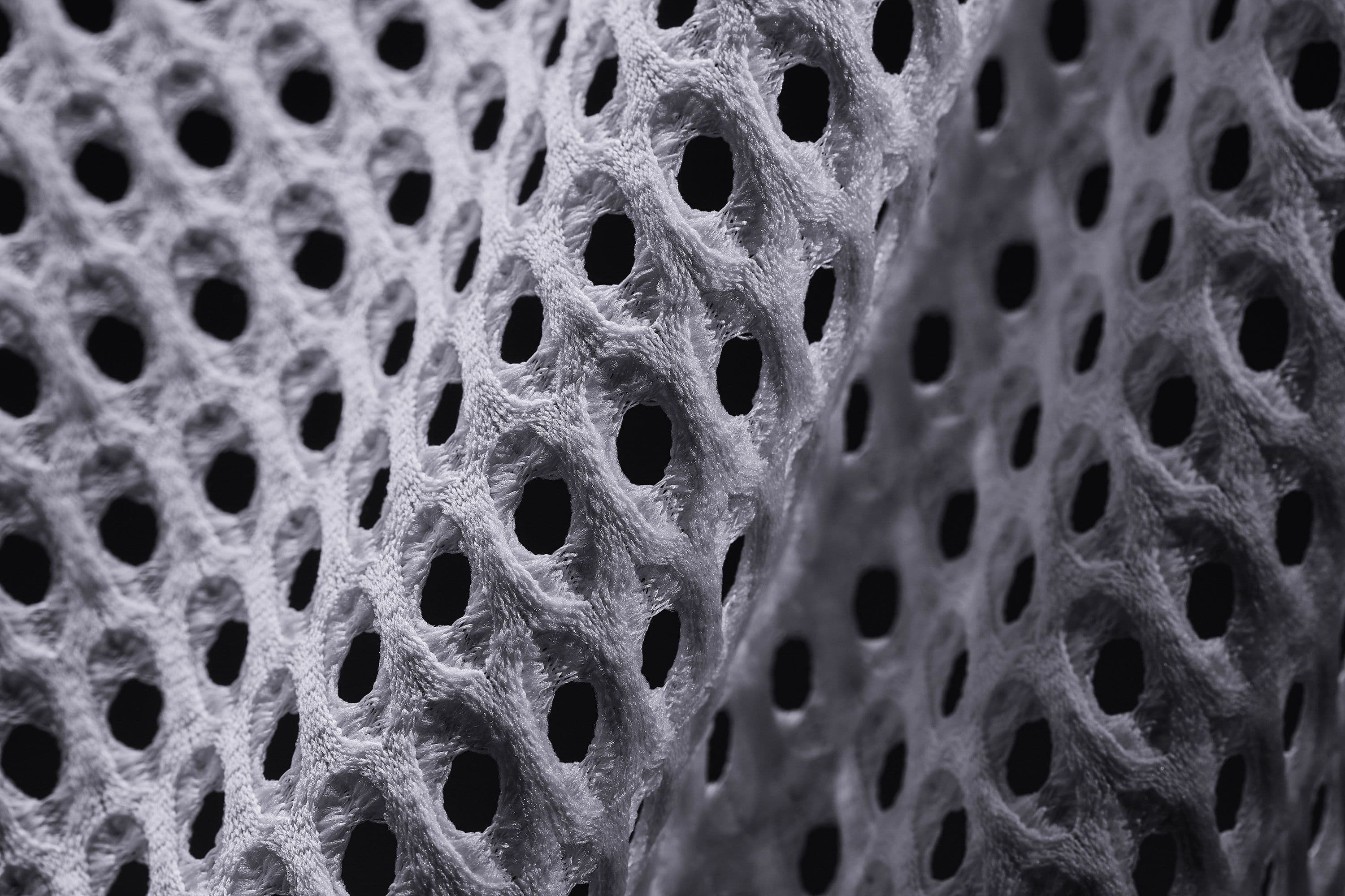 Macro photograph of the Radical AirFlow knit in raking light, a grid of funnel-shaped holes and raised dimples